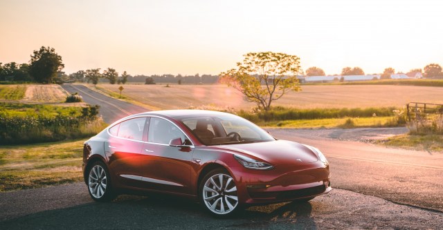 Tesla Model 3 in red parked near fields